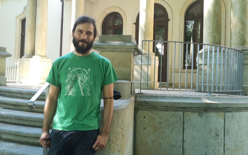 Ein Mann in grünem T-Shirt lehnt an einer Mauer vor einer Villa.