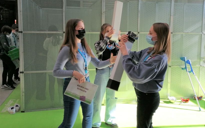 Drei Mädchen experimentieren mit Plastik-Röhren. Im Hintergrund befindet sich das Labyrinth.